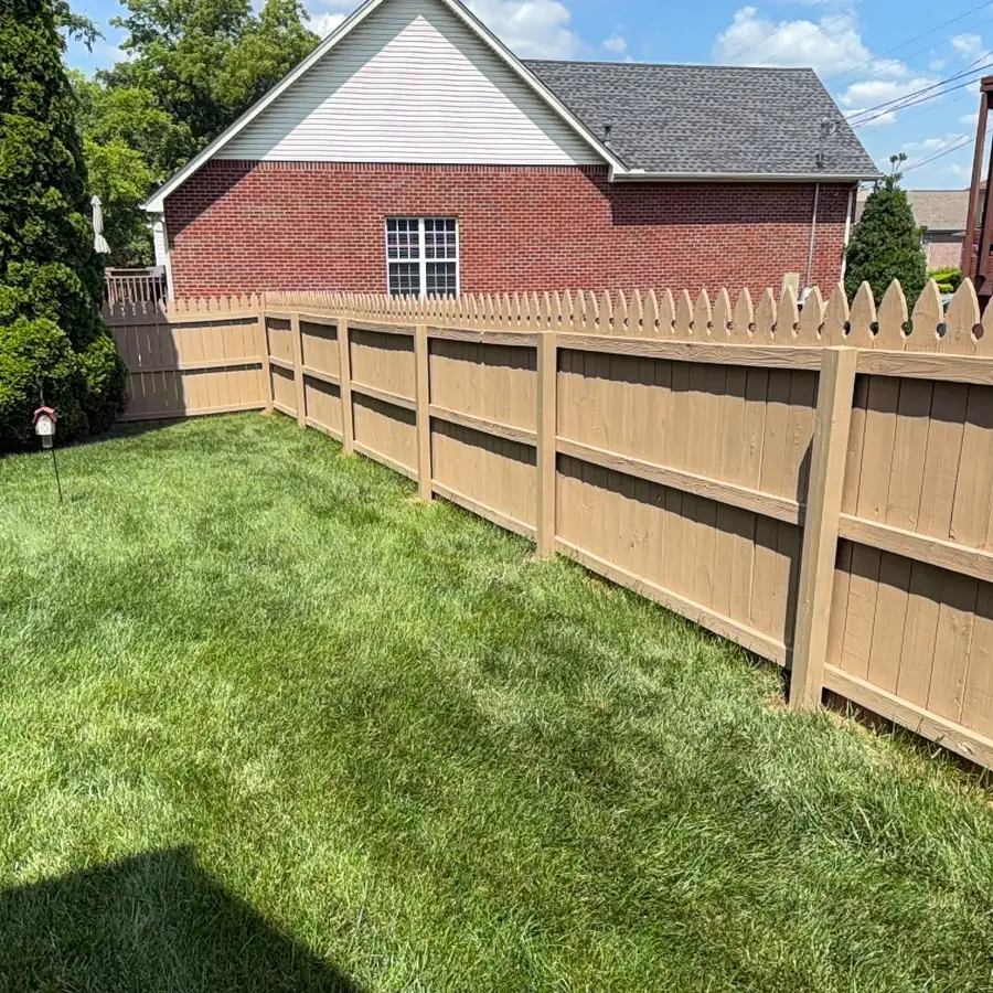 Tan stained wood privacy fence along a lawn beside a brick house